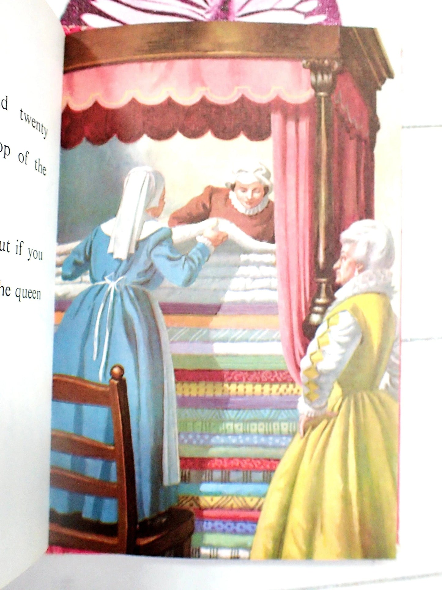 The queen puts lots of mattresses on a four poster bed.