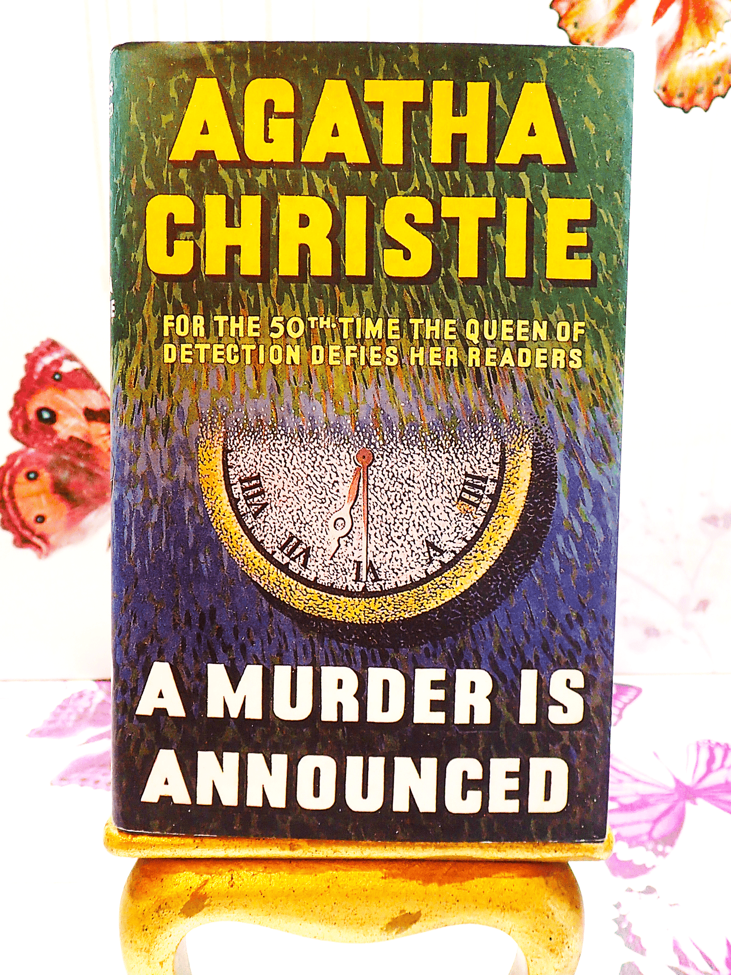 Front cover of Agatha Christie A Murder is Announced showing an image of a clock and titles in vivid yellow.