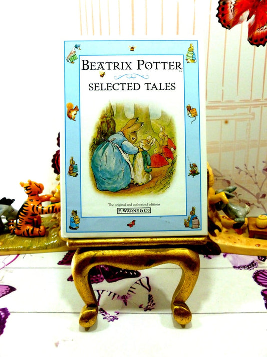 Front cover of vintage book Beatrix Potter Selected Tales showing illustration of Peter Rabbit being dressed by his mother rabbit against a blue ground with other Beatrix Potter characters. 