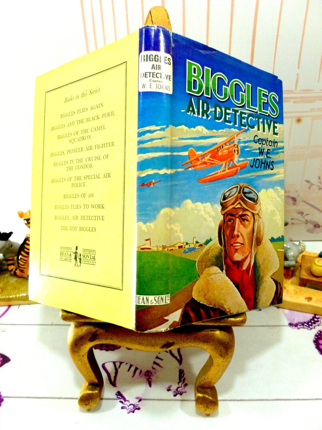Full Cover of Biggles Air Detective Captain W.E. Johns showing Captain Biggles in Flying Uniform with goggles and an aeroplane in the background along with back cover showing other Biggles Titles available in the series.