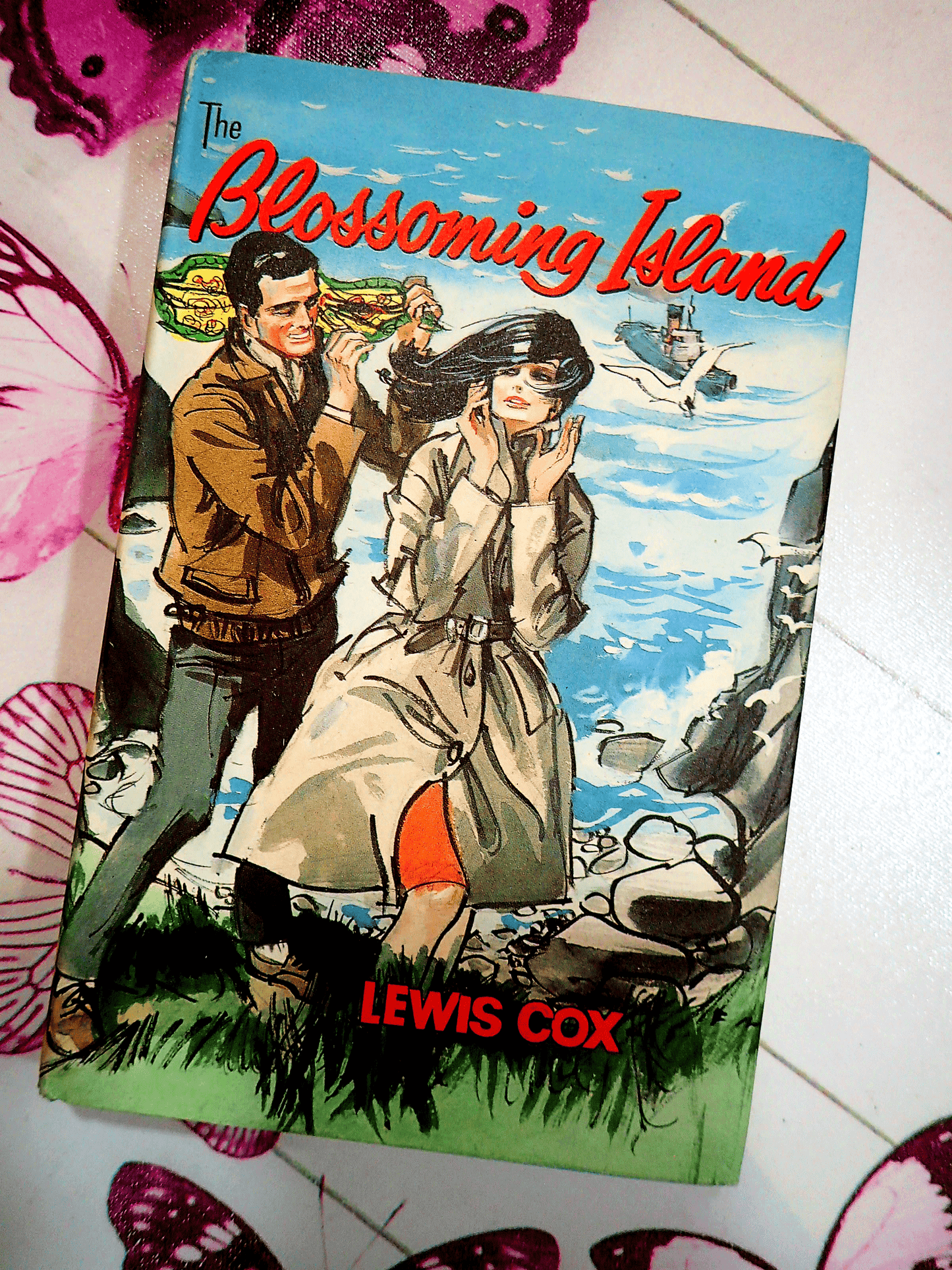Front cover of Blossoming Island Lewis Cox Romance Book Club Hardback showing a man and woman on a cliff top.