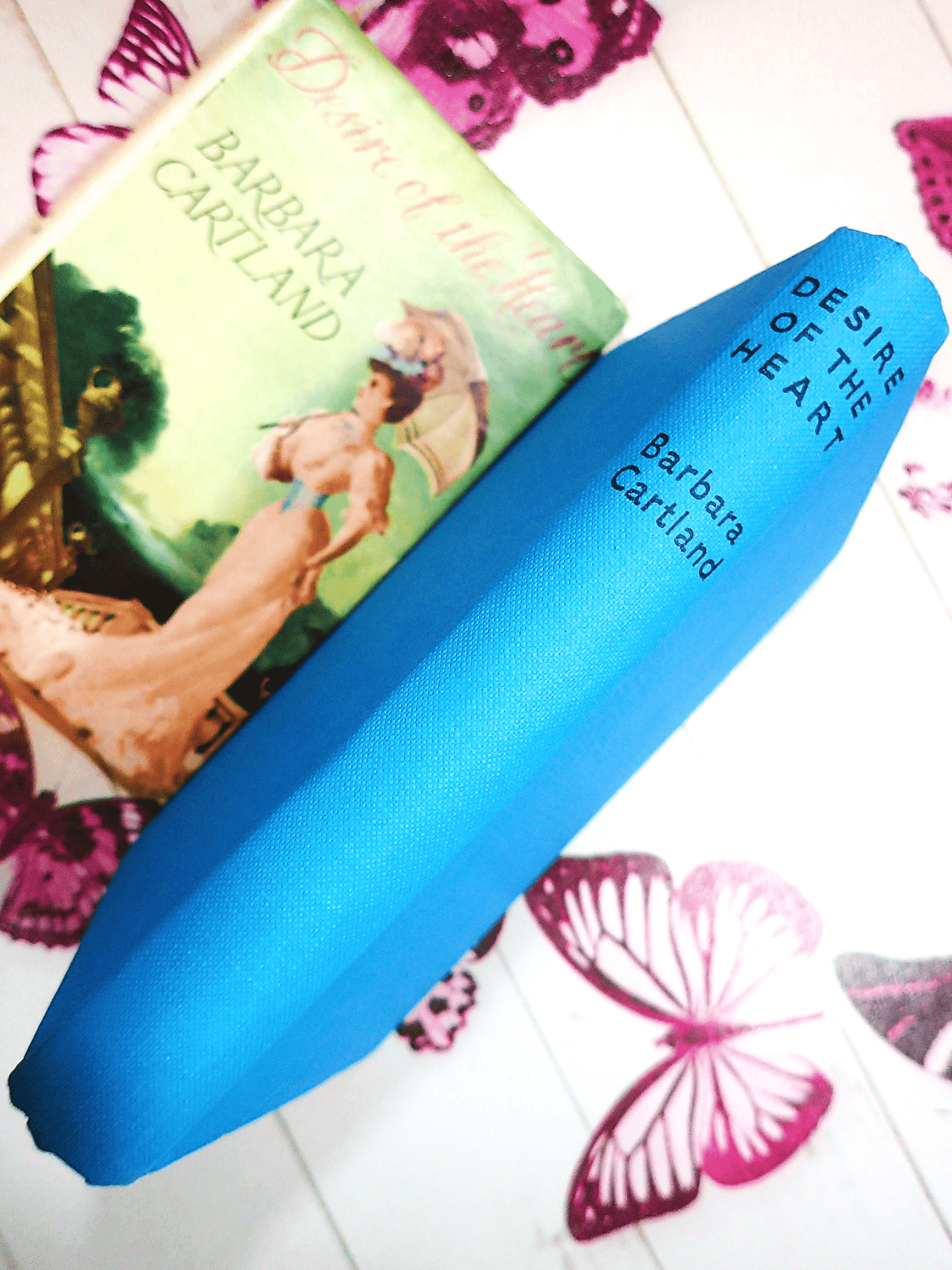 Desire of the Heart Barbara Cartland Hardback showing blue boards with black titles and dust jacket in the background.
