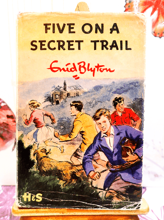 Front cover of Five on a Secret Trail Enid Blyton First Edition 1956 showing Julian, Ann, Dick, George and Timmy the dog running away from something. 