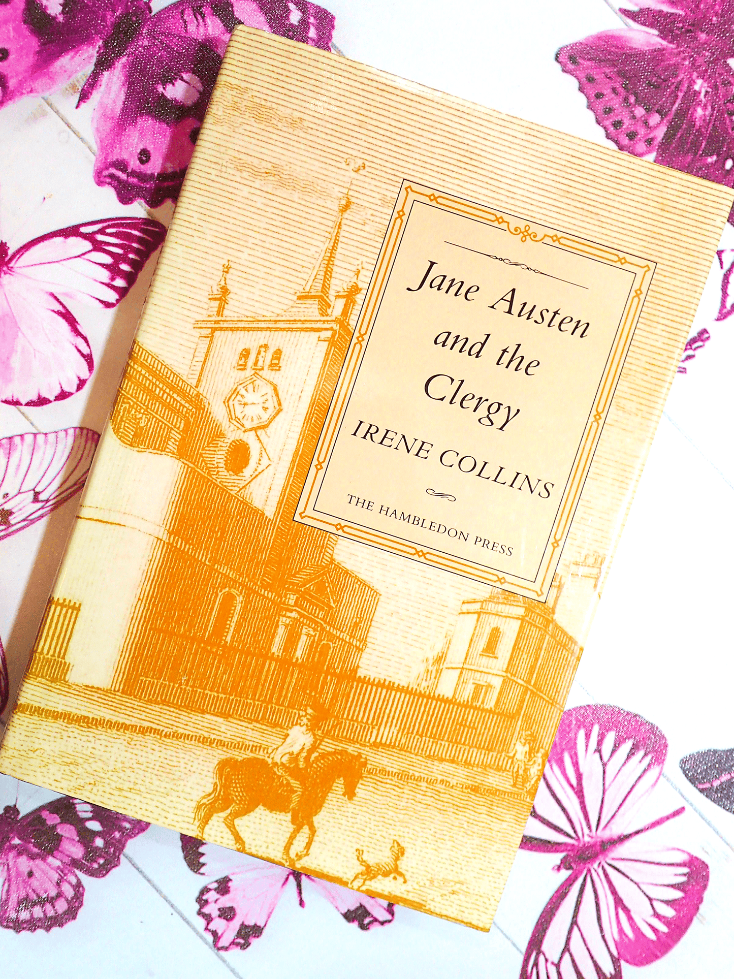 Front cover of vintage book Jane Austen and the Clergy by Irene Collins showing a sepia engraving of a Regency street against a butterfly background.