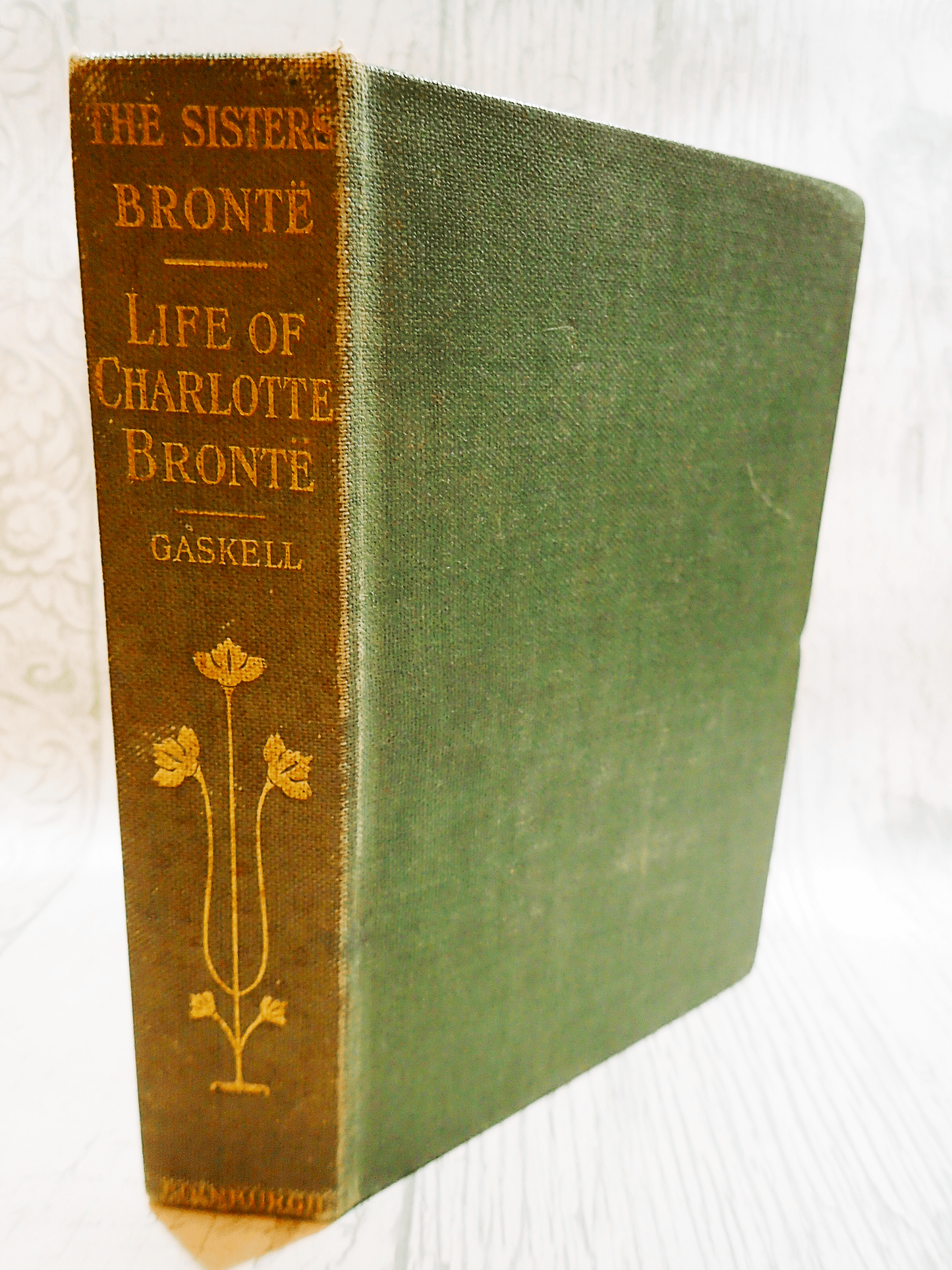 Spine and front cover of antique book The Life of Charlotte Bronte by Mrs Gaskell 1907 with decorative gilt titles on sage green cloth covered boards.