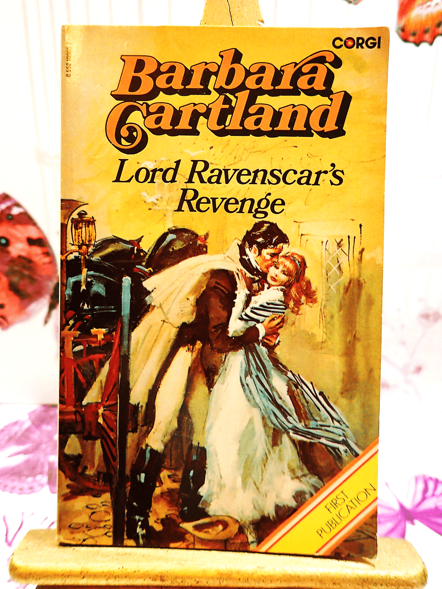 Front cover of Lord Ravenscar's Revenge Barbara Cartland Corgi Paperback showing a handsome man in a cape kissing a lady in 19th century dress.