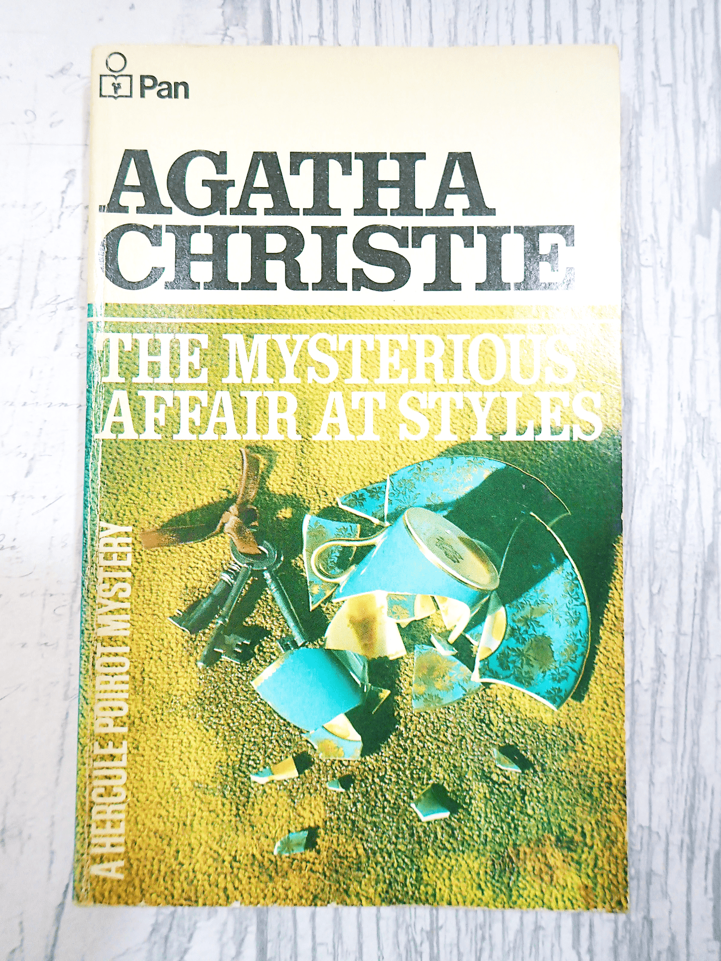 Front cover of Agatha Christie's book The Mysterious Affair at Style, Vintage Pan Paperback, showing a broken coffee cup on the carpet next to a bunch of keys. Against a light background.