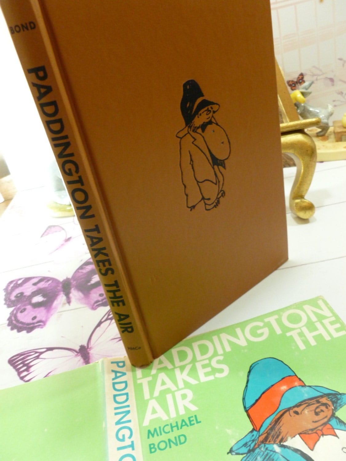 Tan cloth covered boards of Paddington Takes the Air Vintage Book First American Edition showing Paddington Bear illustration and black titles to the spine.
