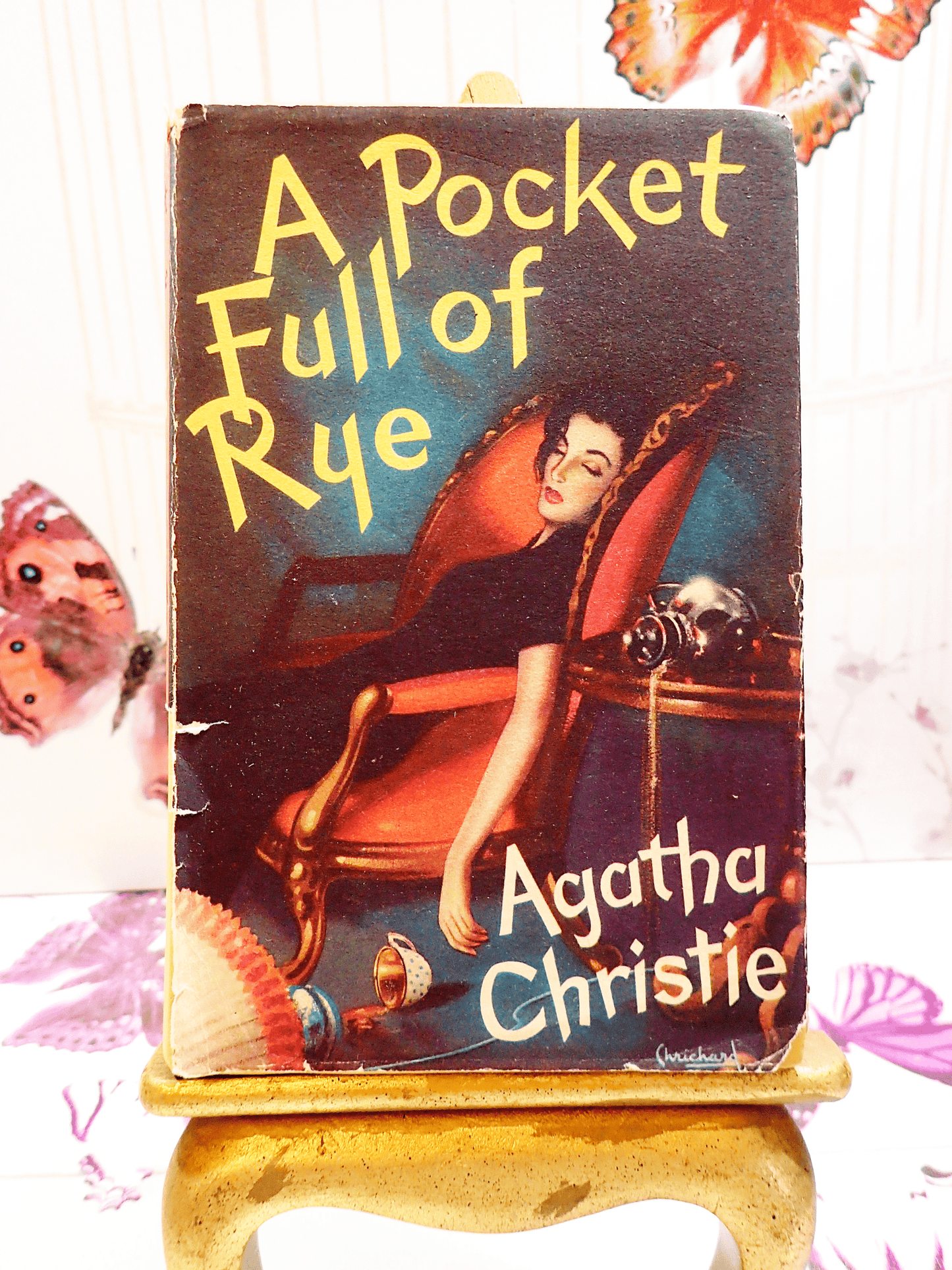 Front cover of A Pocketful of Rye Agatha Christie Vintage Thriller Book Club First Edition 1954 Showing a woman collapsed in a chair with a spilled coffee cup next to her in dramatic colours.