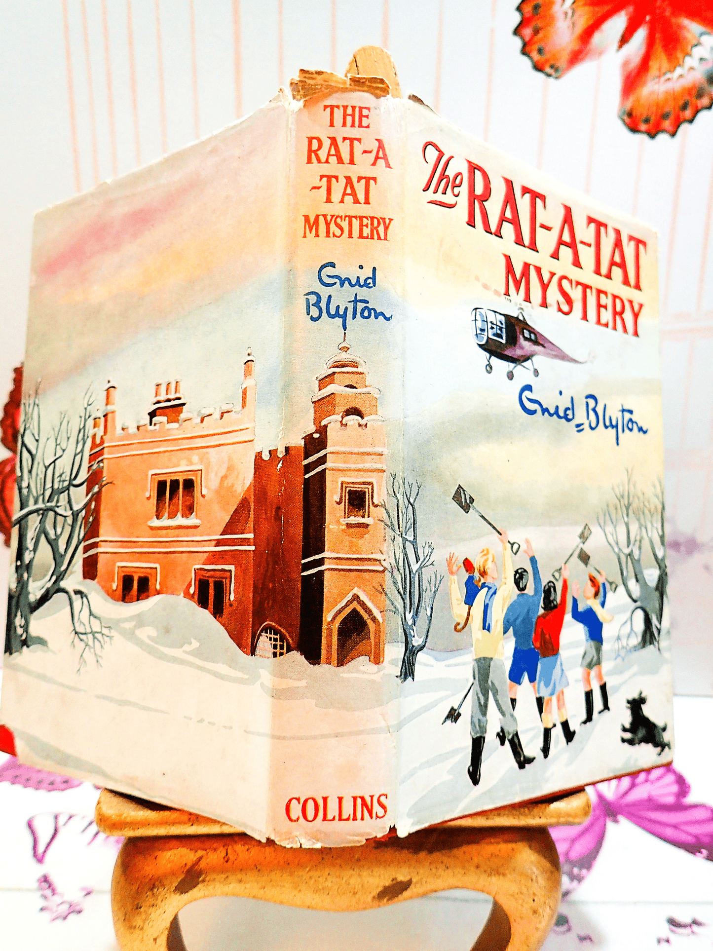 Cover and Spine of The Rat-A-Tat Mystery by Enid Blyton Vintage Children's Book Collins First Edition 2nd Imp. showing children in a snowy landscape near a castle and title to the spine.