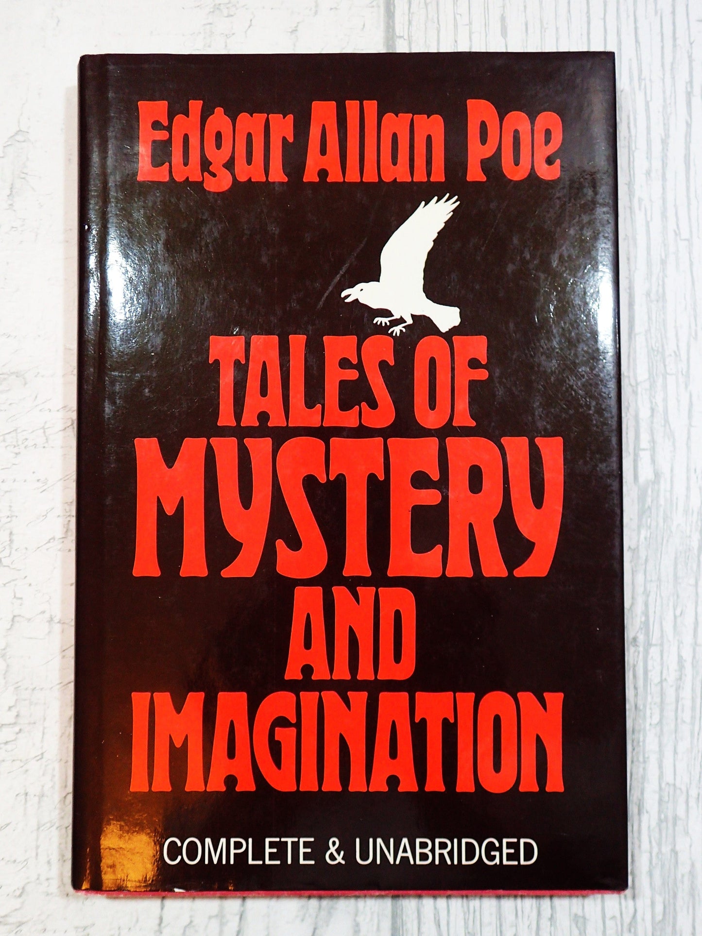 Front cover of Tales of Mystery and Imagination Edgar Allan Poe Vintage Book 1980's showing a white raven and scarlet red titles against a black ground displayed on a light background.