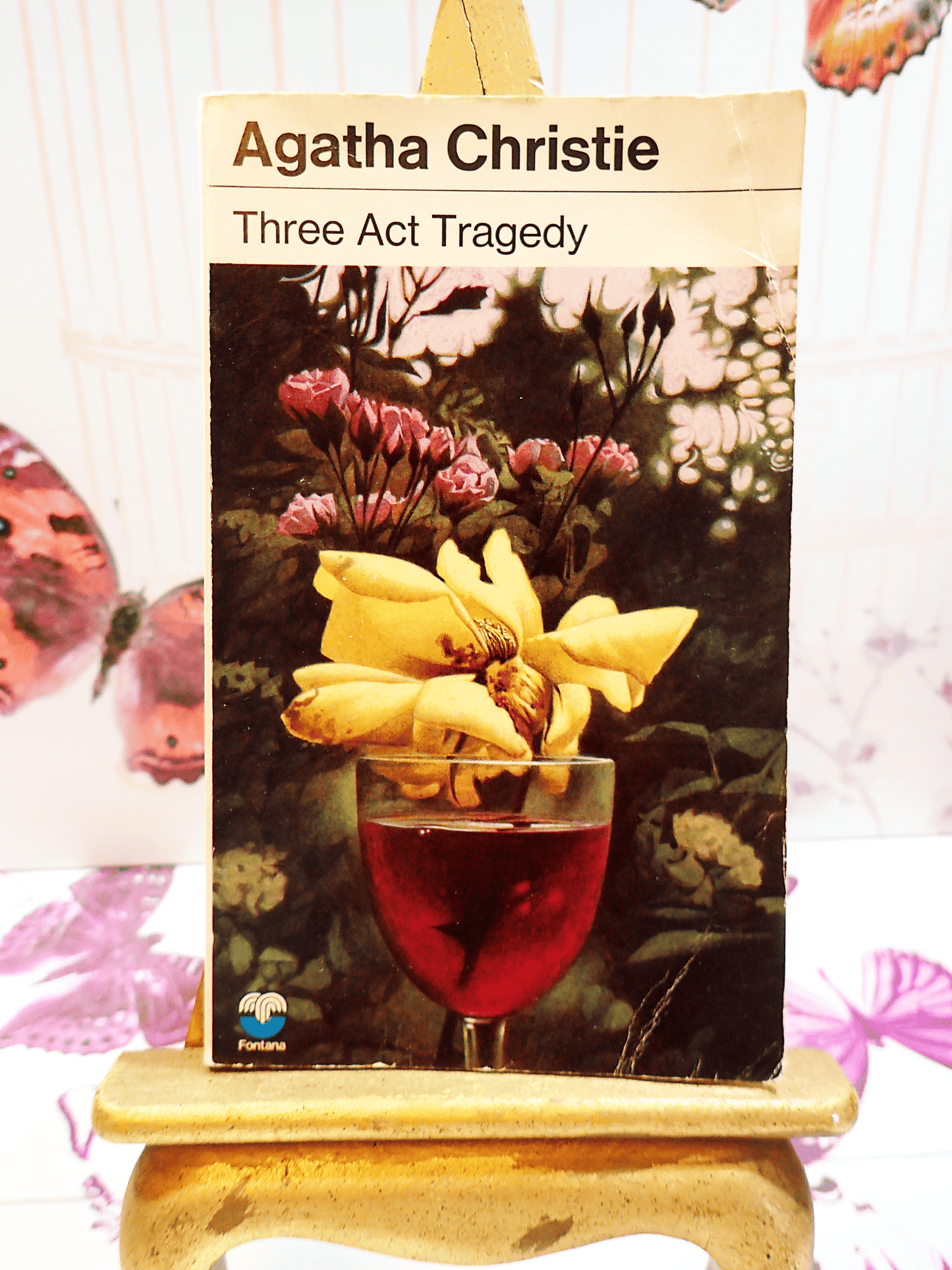 Front cover of Three Act Tragedy by Agatha Christie Vintage Pan Paperback Classic Crime book showing a flower with yellow petals in a glass of red wine.