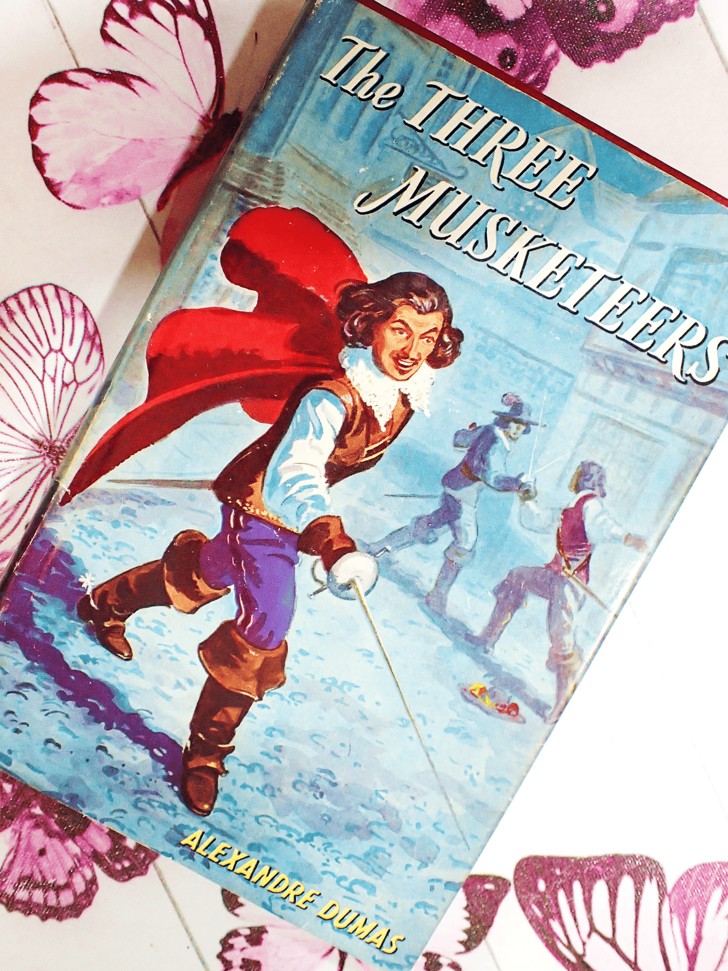 The Front cover of the Three Musketeers by Baroness Orczy vintage book showing a dashing D'artagnan holding a sword.
