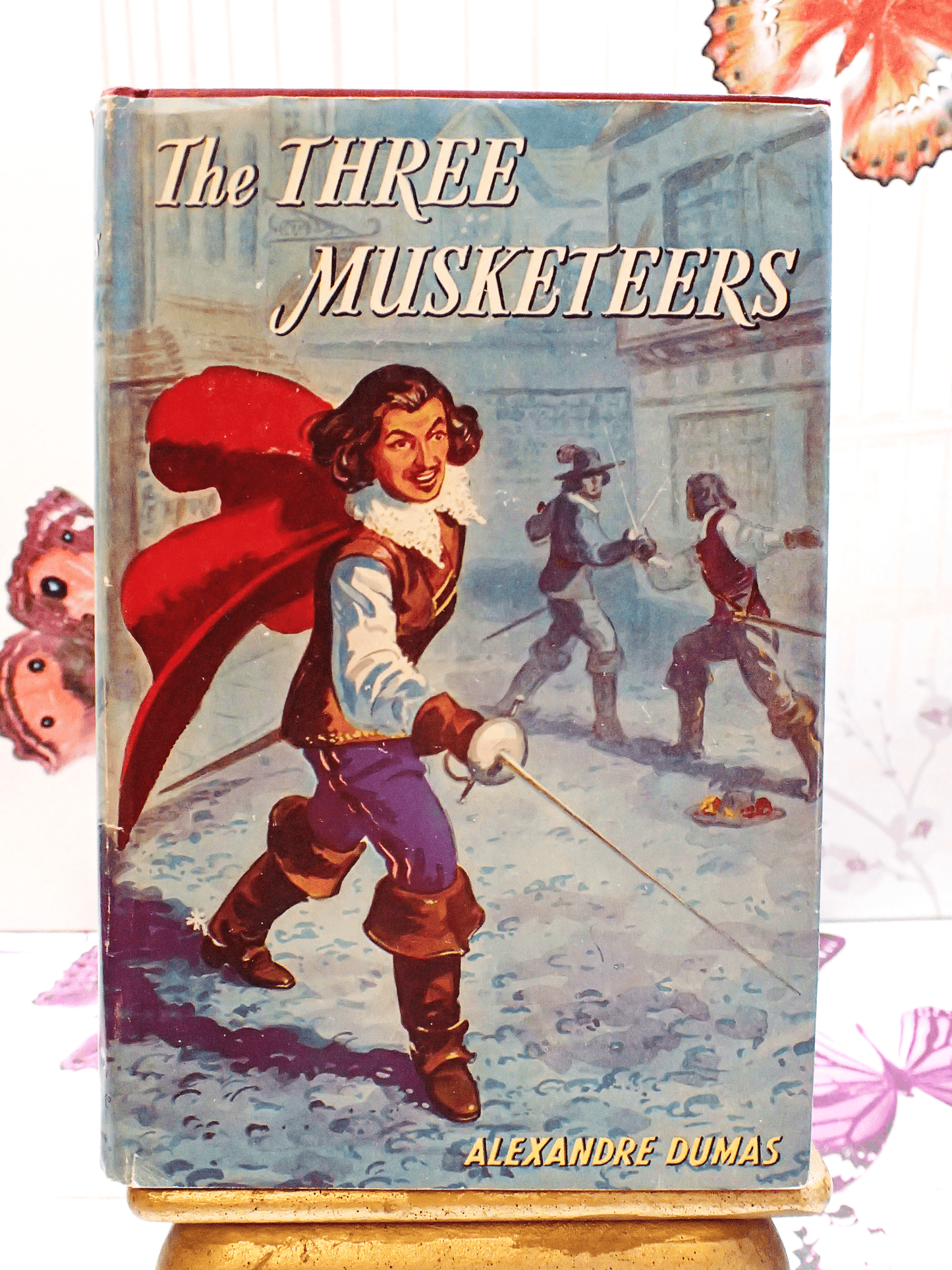 The Front cover of the Three Musketeers by Baroness Orczy vintage book showing a dashing D'artagnan holding a sword.