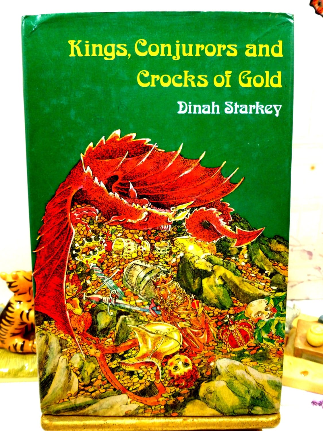 Front cover of Kings Conjurors and Crocks of Gold 1975 folk tale book with colourful dragon on its hoard against a green ground.