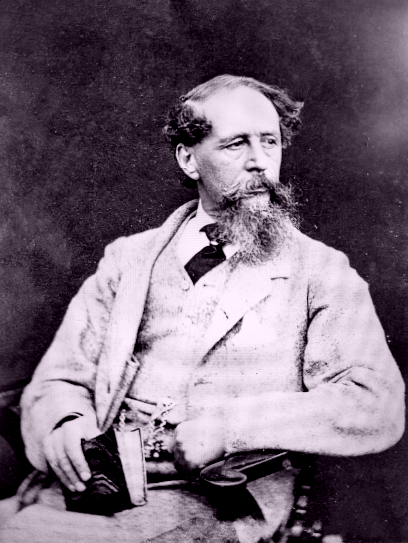 Charles Dickens holding a book wearing a suit with Albert Chain Tie and sporting handlebar moustache and whiskers. Black and White Photograph.
