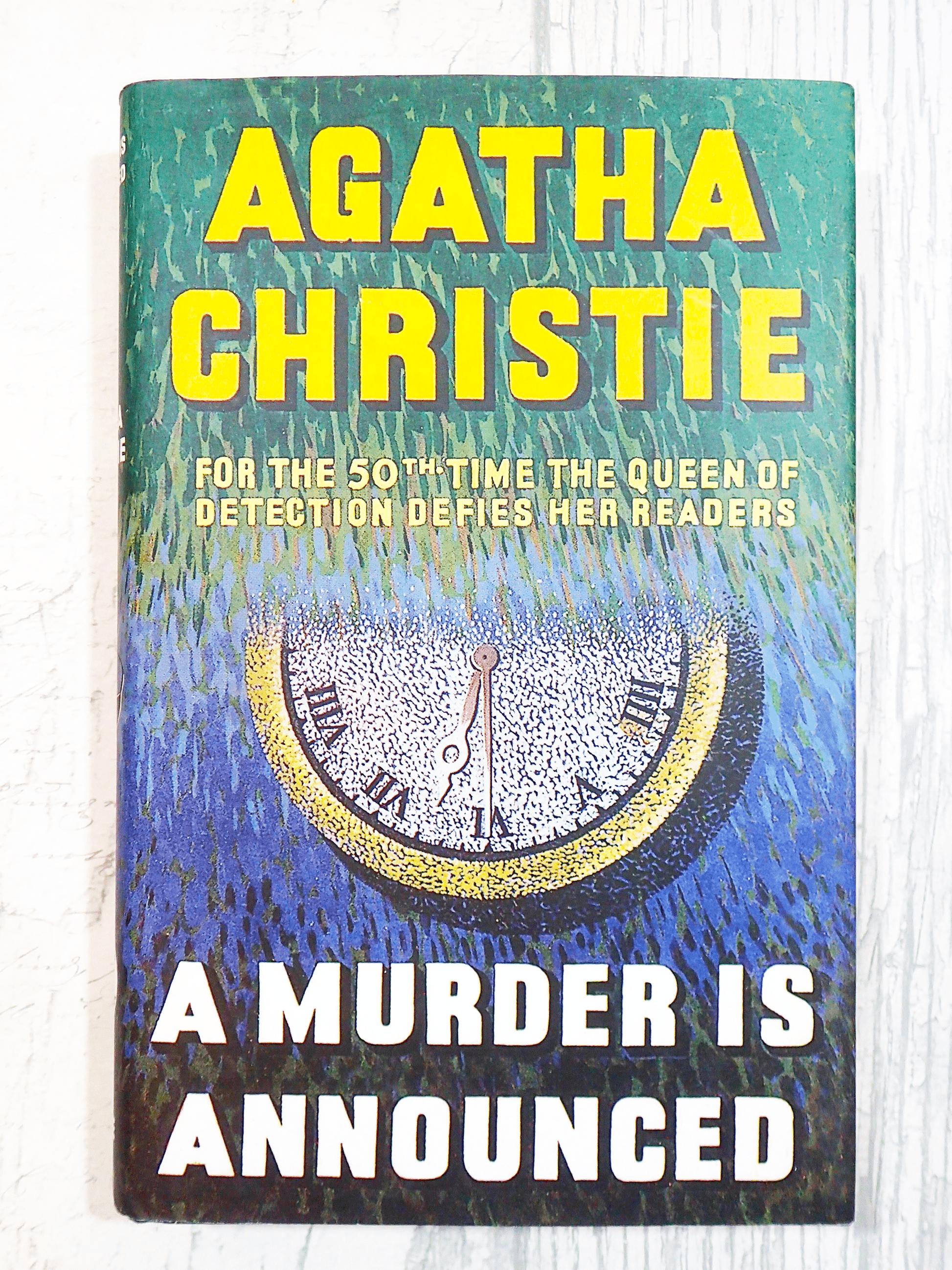 Front cover of Agatha Christie A Murder is Announced showing an image of a clock and titles in vivid yellow. 