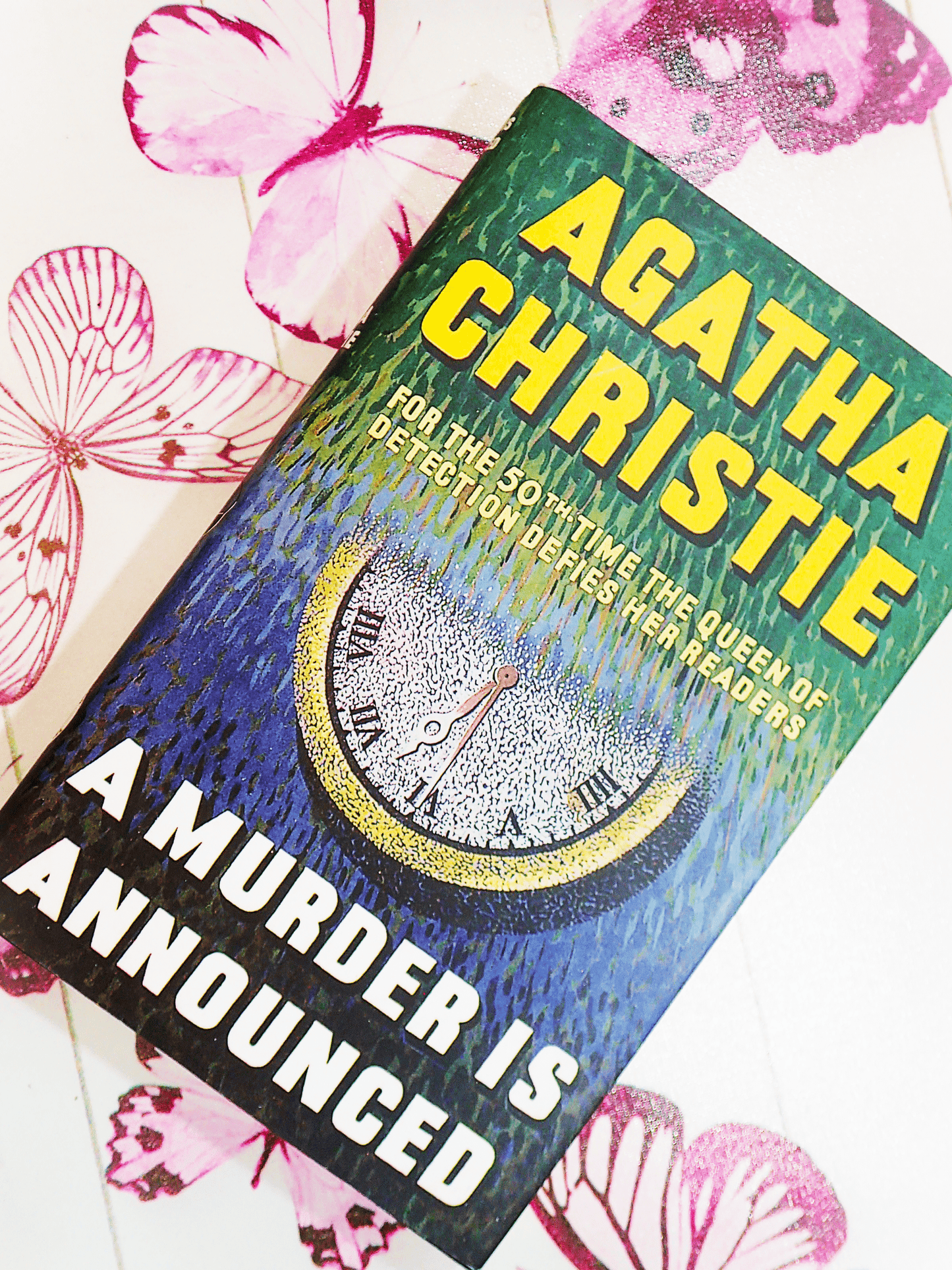 Front cover of Agatha Christie A Murder is Announced showing an image of a clock and titles in vivid yellow against a background of butterflies. 