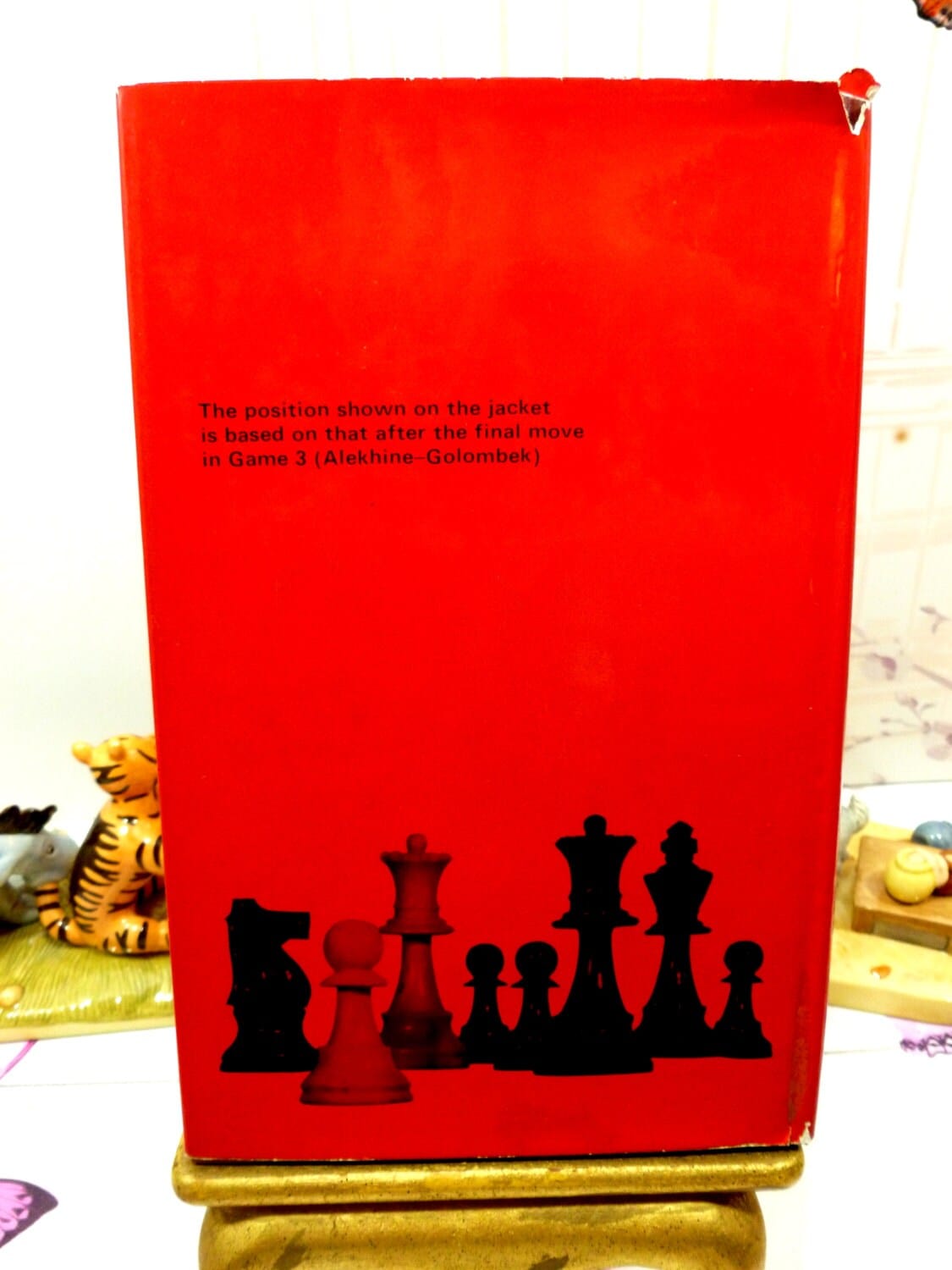 Back cover of dust jacket of Alekhines Best Games of Chess 1938-45 Hardback in red showing black images of chess pieces. 