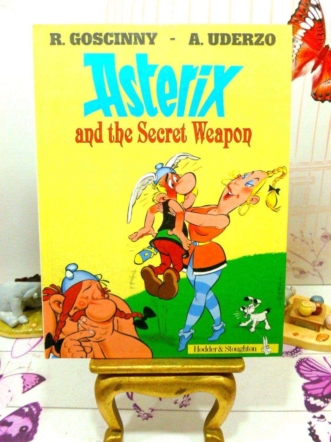 Front cover of Asterix and the Secret Weapon Goscinny Uderzo the Gaul series First English Edition 1991 showing Asterix being hugged by a tall blond woman.