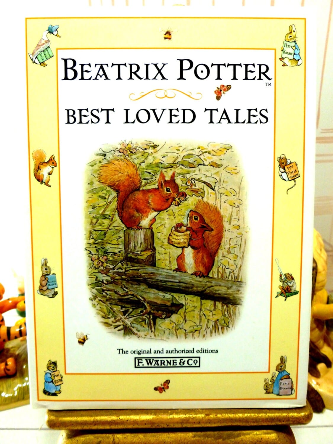 Front cover of Beatrix Potter Best Loved Tales showing Squirrel Nutkin and a squirrel holding a basket against a yellow ground illustrated with other Beatrix Potter Characters. 