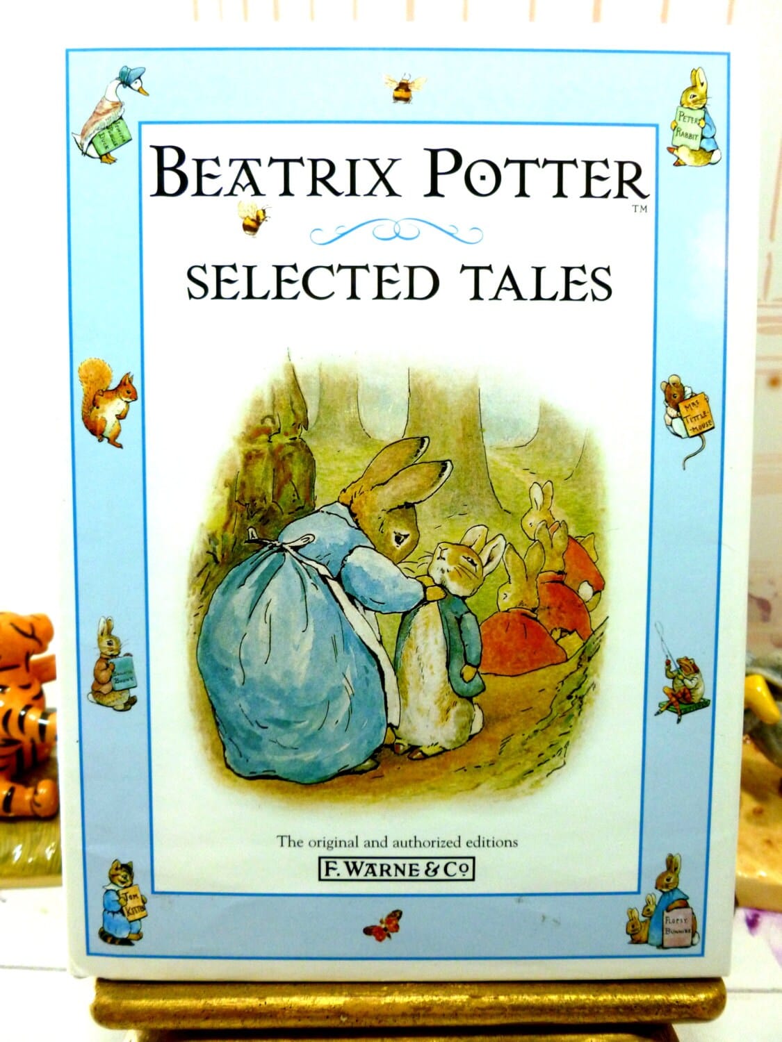 Front cover of vintage book Beatrix Potter Selected Tales showing illustration of Peter Rabbit being dressed by his mother rabbit against a blue ground with other Beatrix Potter characters. 