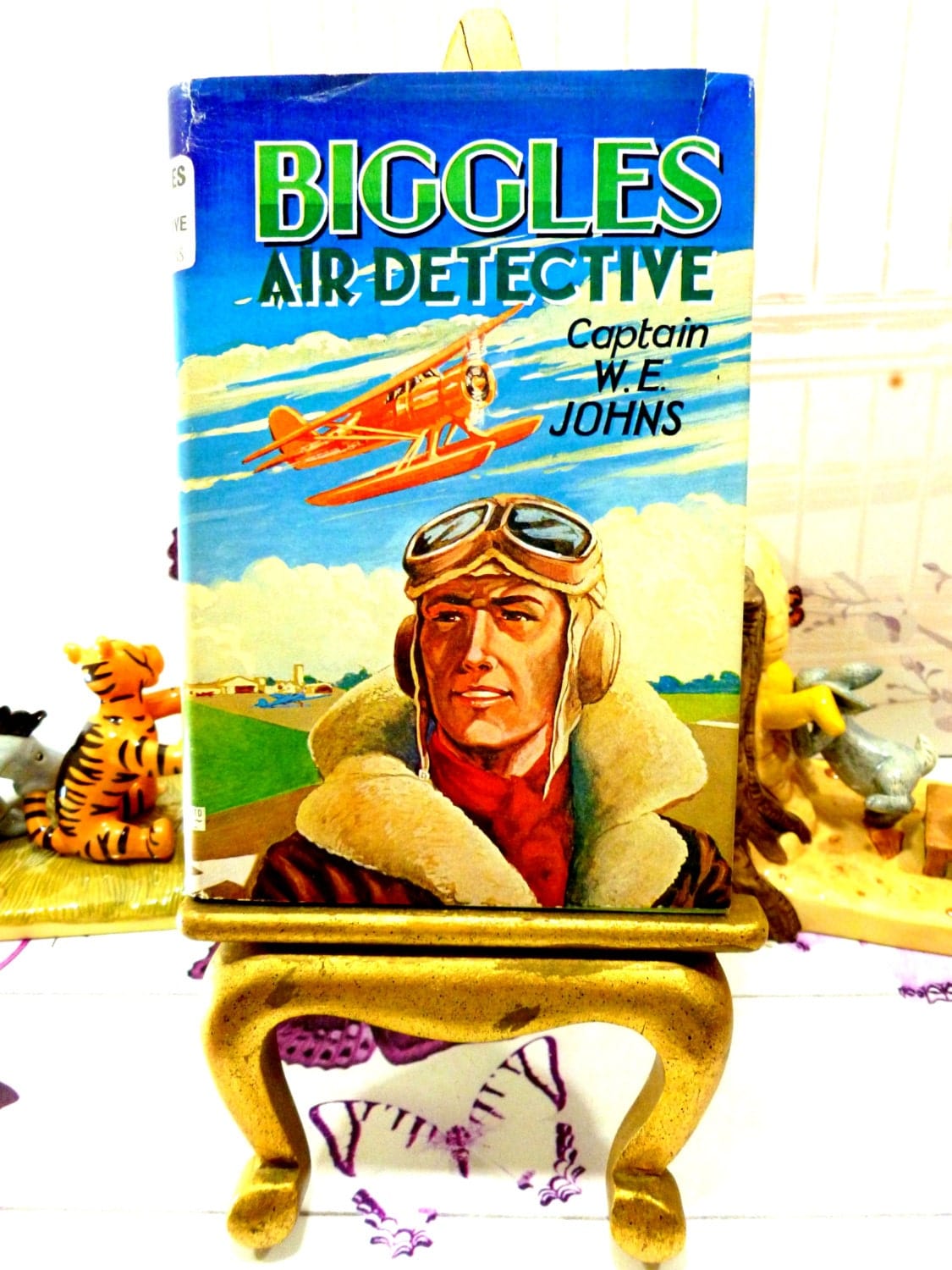 Front Cover of Biggles Air Detective Captain W.E. Johns showing Captain Biggles in Flying Uniform with goggles and an aeroplane in the background. 