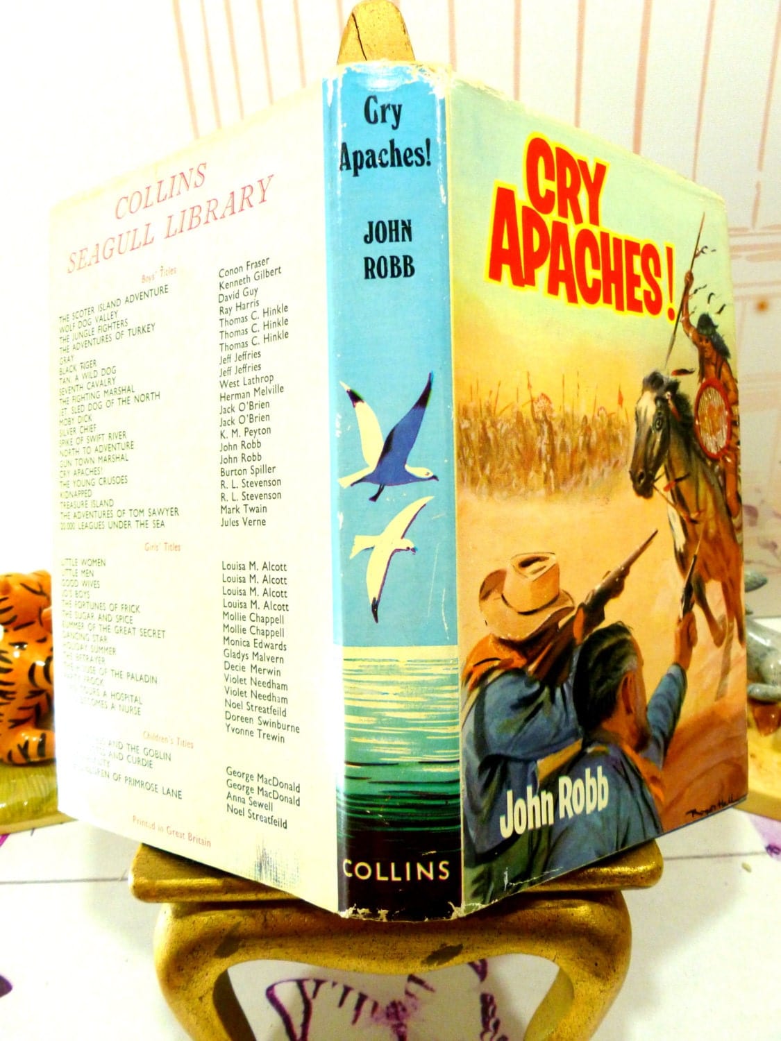 Full cover of Cry Apache Catsfoot Cowboy Stories 1960s Vintage Hardback chldren's book showing cowboys fighting an Indian and other titles from the series on the back cover. 