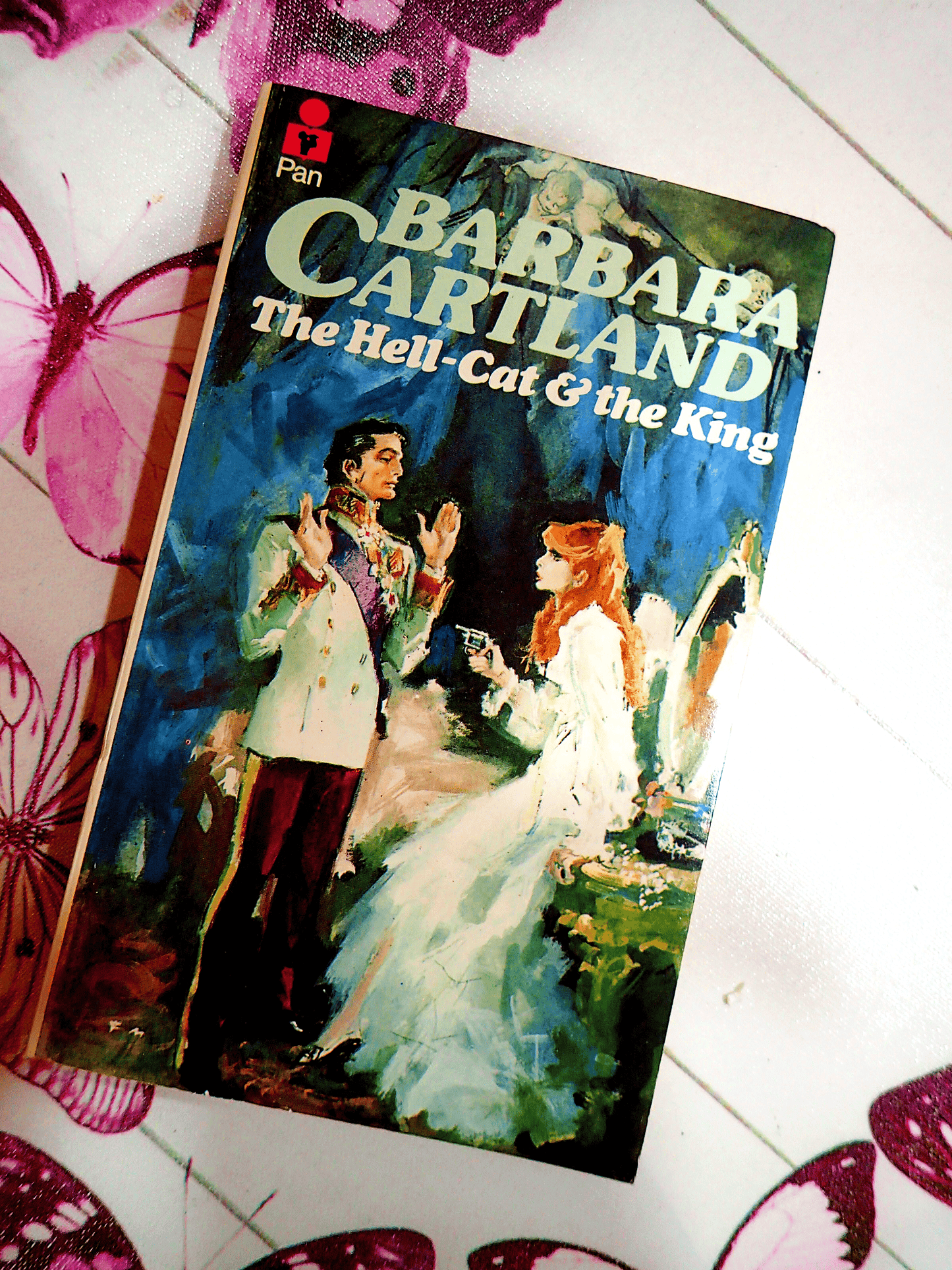 Cover of The Hell Cat and the King Barbara Cartland Pan Paperback First Edition showing a red haired woman pointing a gun at a handsome aristocrat. 