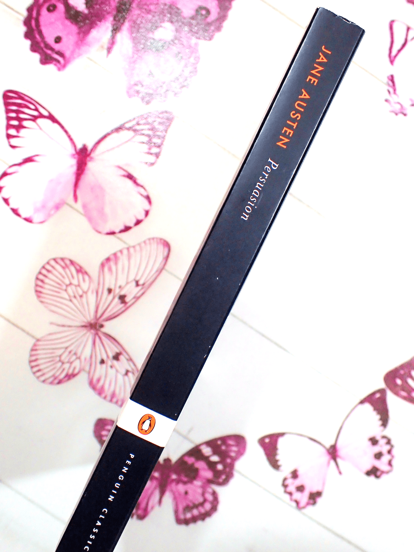 Spine of Penguin Classic Paperback Persuasion Austen showing orange and white titles on black against a butterfly background. 