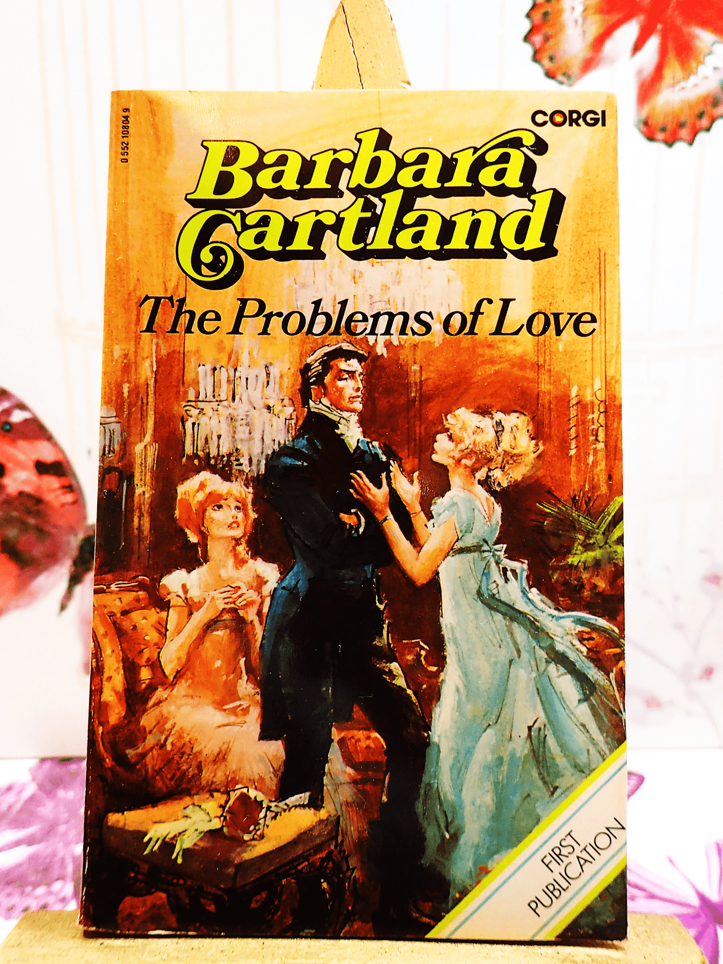 Front cover of The Problems of Love Barbara Cartland Corgi first edition showing a pretty woman in a blue dress pleading with a handsome man. 