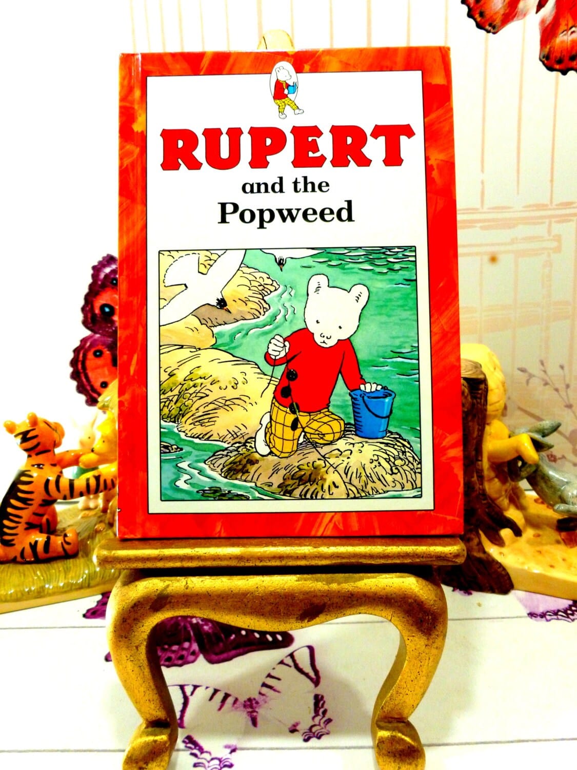 Front cover of Rupert and the Popweed Vintage Hardback Rupert Book 1st Ed 1991 showing Rupert and a Seagull against a red border. 