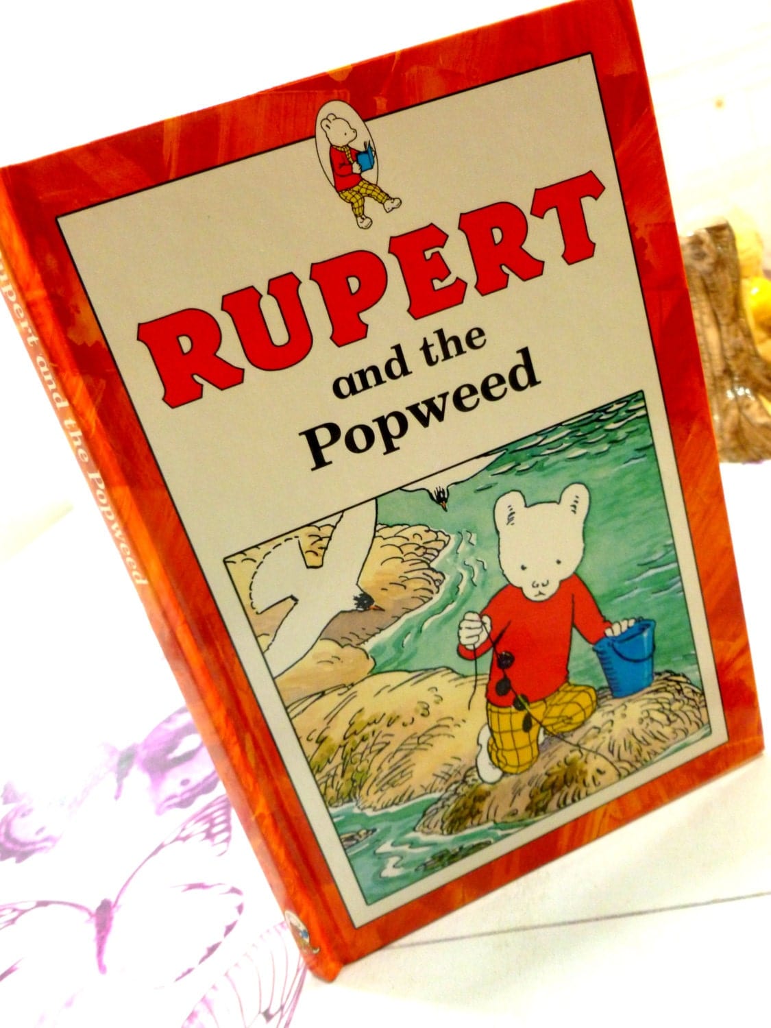 Front cover of Rupert and the Popweed Vintage Hardback Rupert Book 1st Ed 1991 showing Rupert and a Seagull against a light background. 