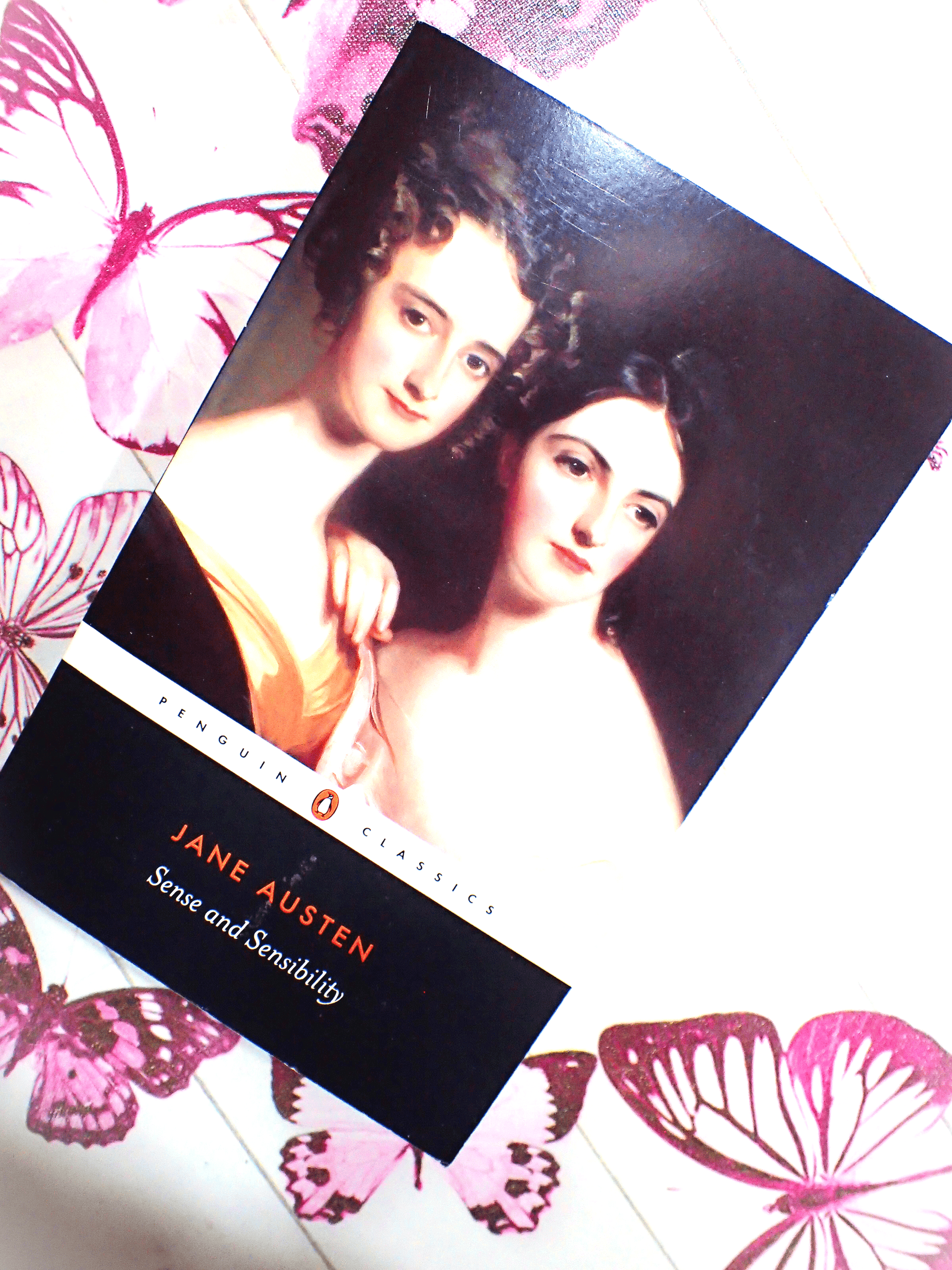 Front cover of paperback book Penguin Classics Sense and Sensibility Jane Austen showing portrait of two Regency ladies against a butterfly background. 