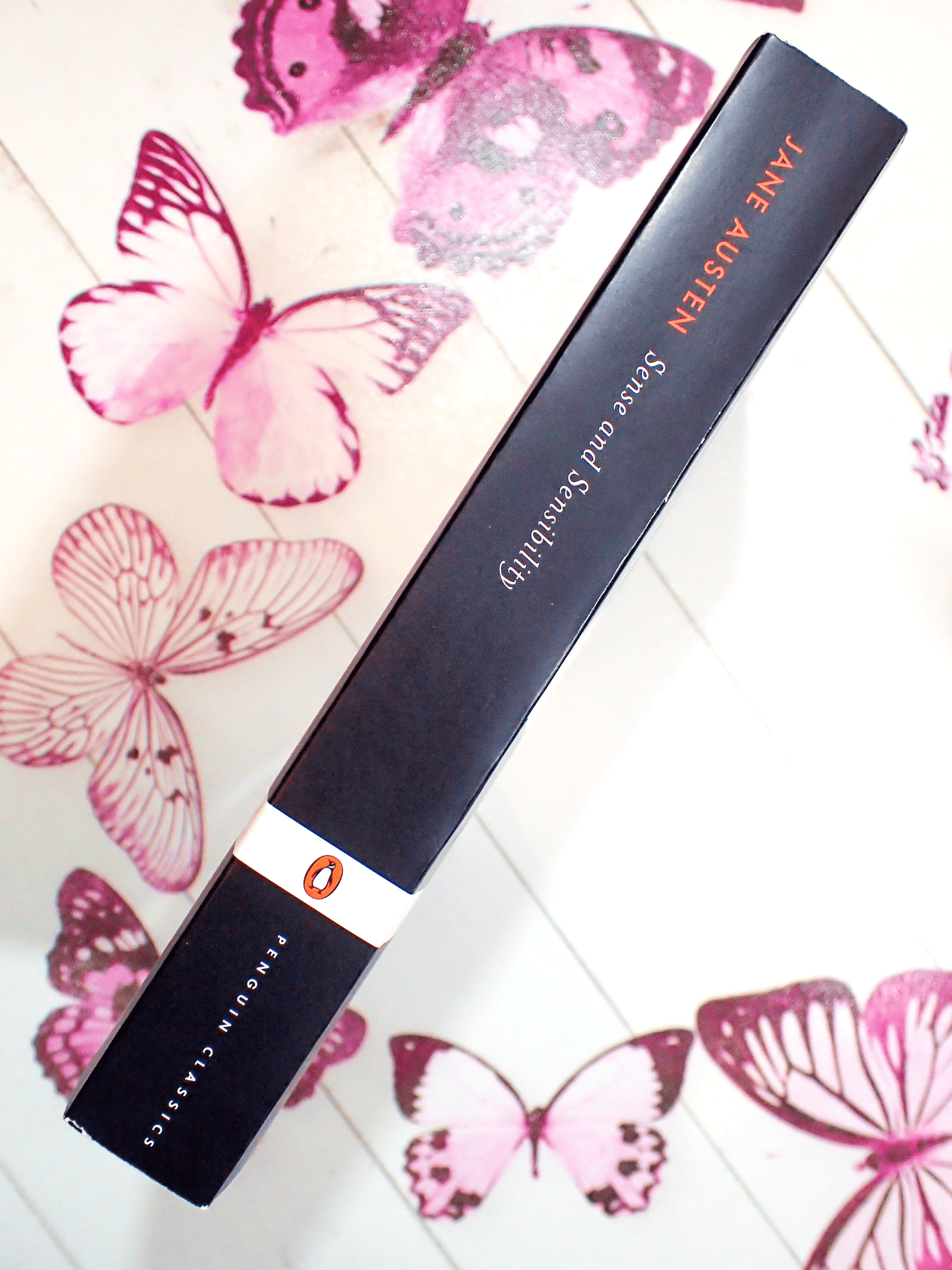 Spine of paperback book Penguin Classics Sense and Sensibility Jane Austen showing orange and white titles against black on a butterfly background. 
