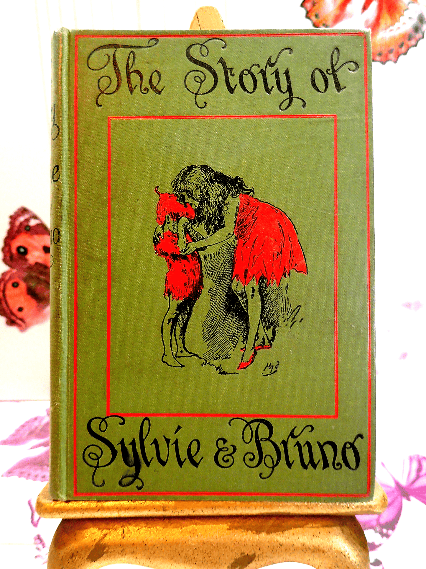 Front cover of The Story of Sylvie and Bruno Lewis Carroll Vintage Green and Red Hardback Book Macmillan showing Sylvie tallking to a fairy. 