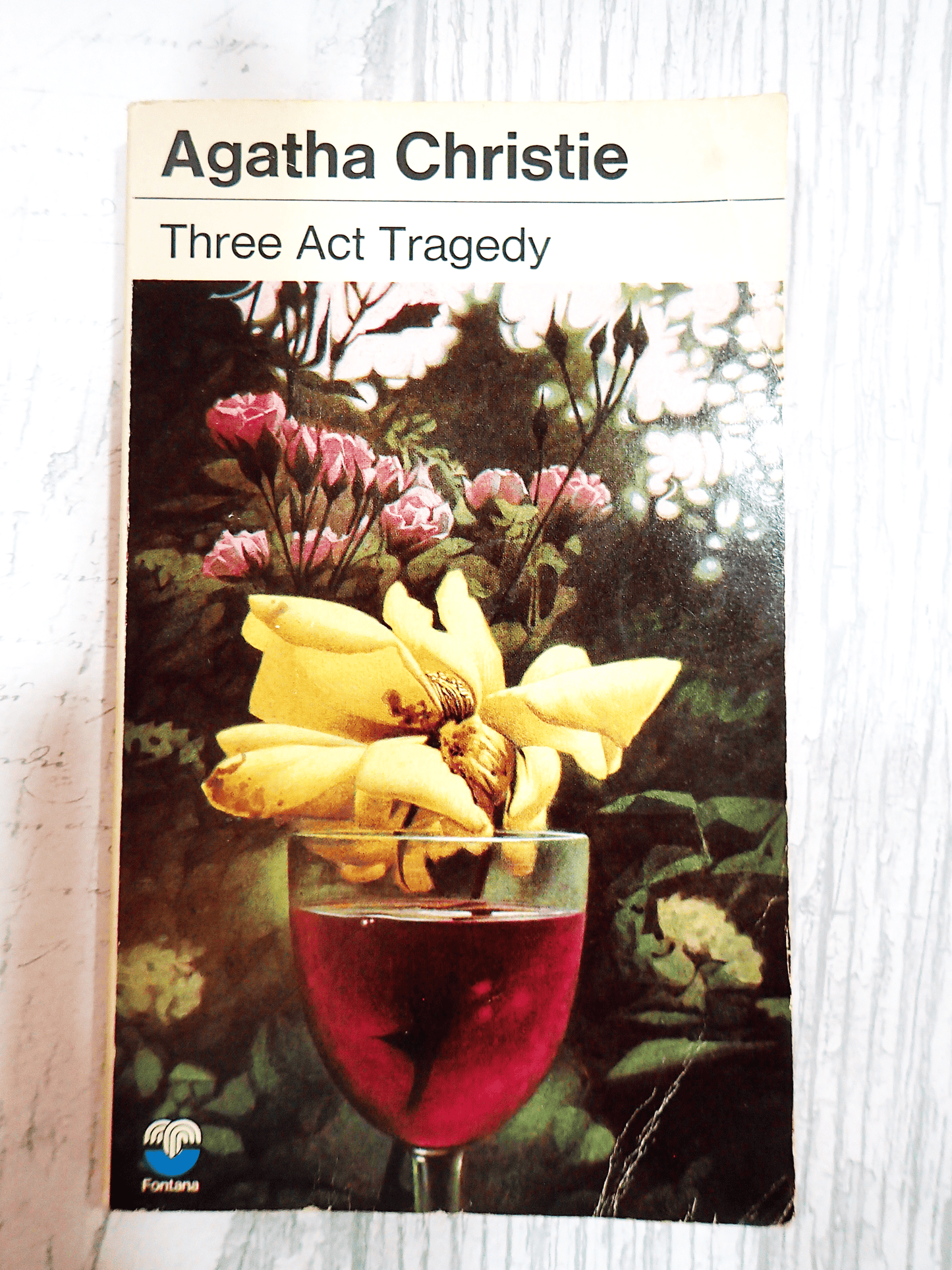 Front cover of Three Act Tragedy by Agatha Christie Vintage Pan Paperback Classic Crime book showing a flower with yellow petals in a glass of red wine against a light background