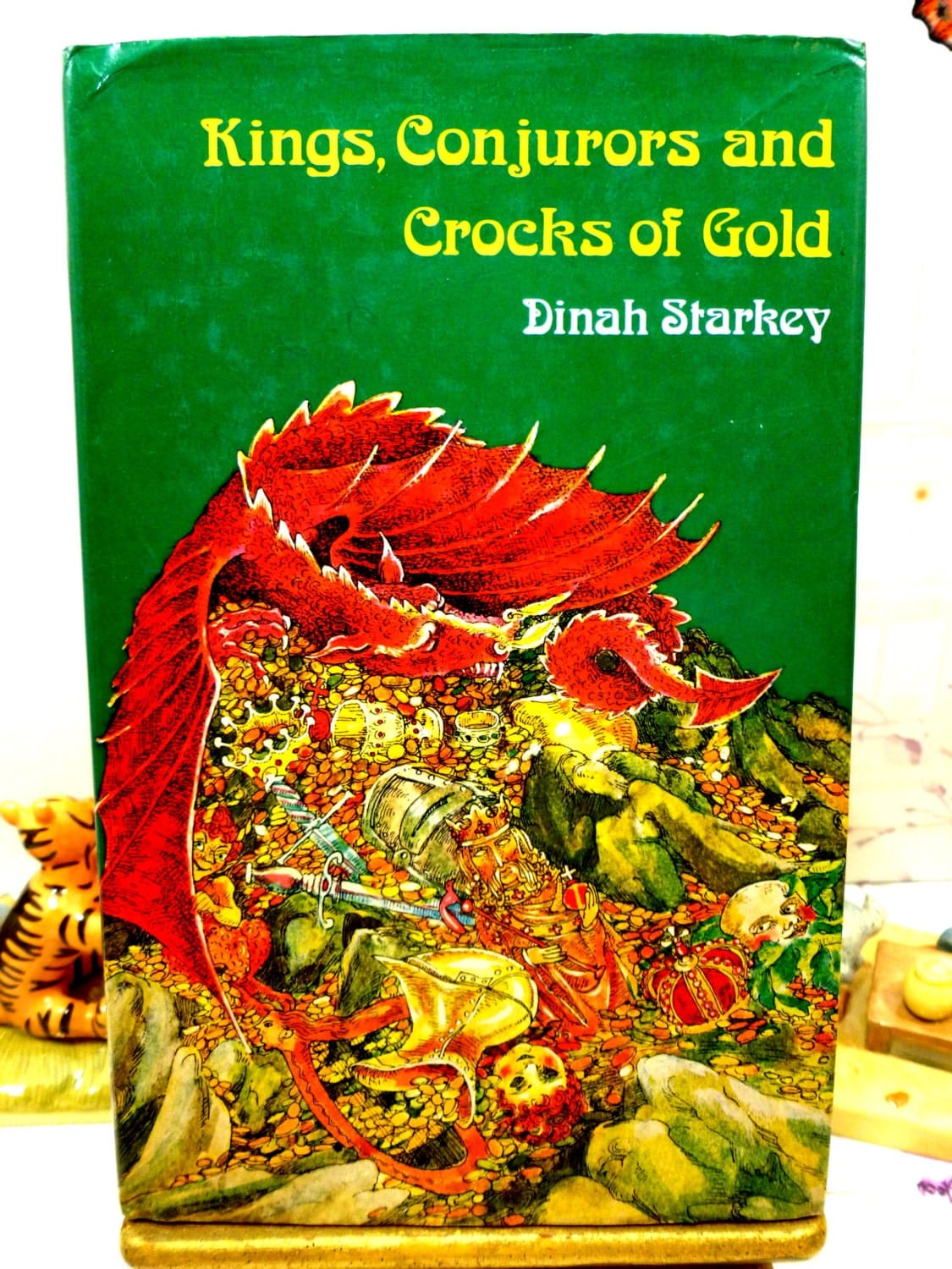 Front cover of Kings Conjurors and Crocks of Gold 1975 folk tale book with colourful dragon on its hoard against a green ground. 